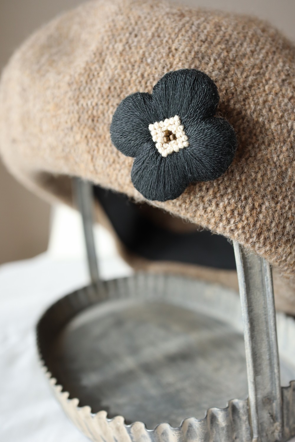 ベージュの帽子につけた黒い花の刺繍ブローチ
